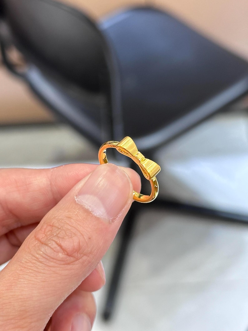 A gold ring with a bow on it is being held in a person's hand.