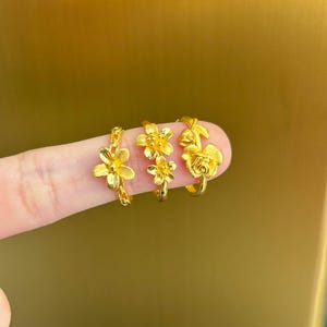 A close-up image of a person's finger wearing three gold-colored flower-shaped rings.