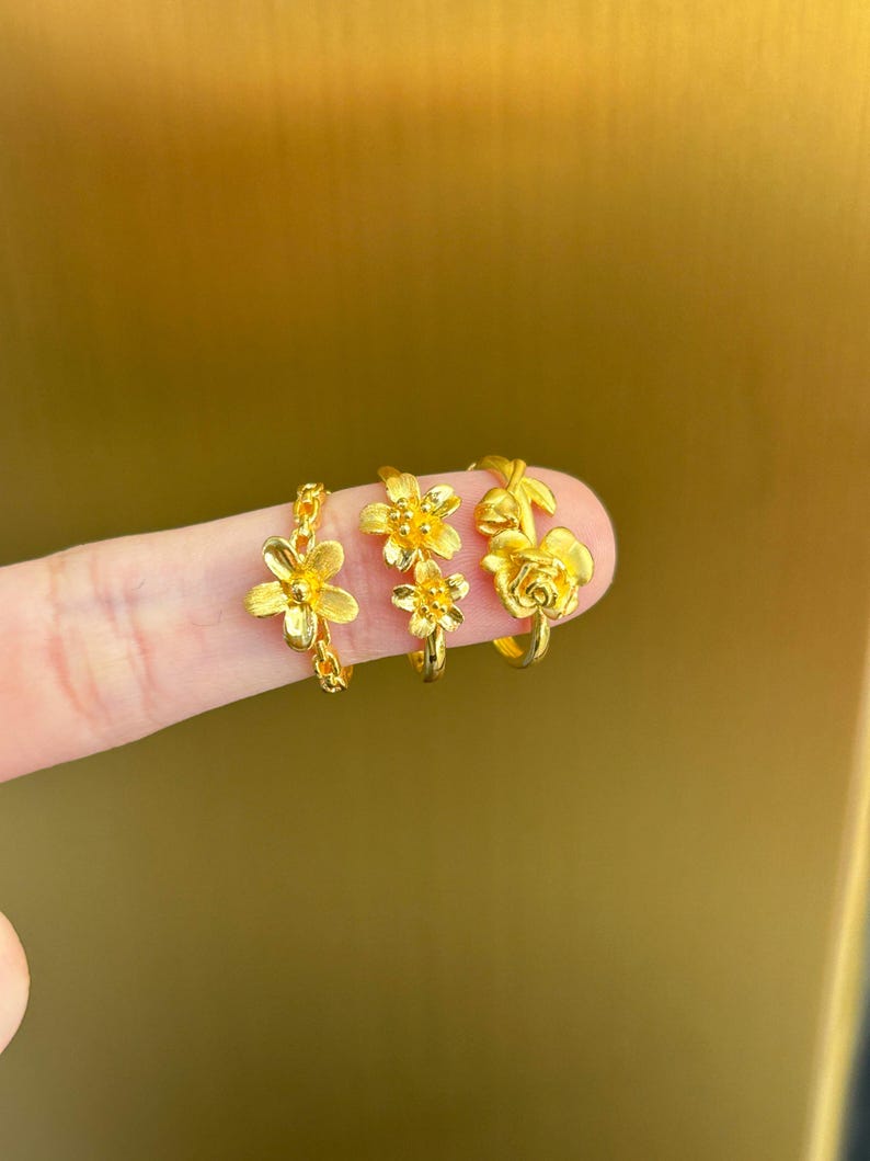 A close-up image of a person's finger wearing three gold-colored flower-shaped rings.