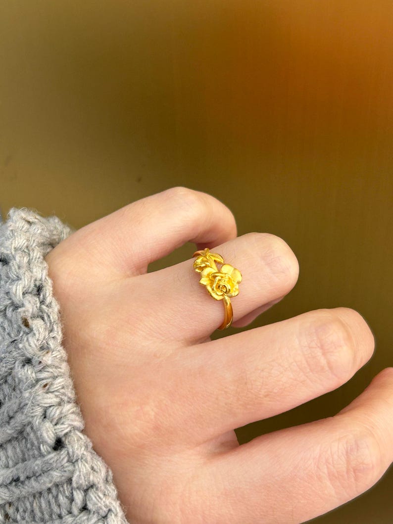 A close-up view of a person's hand wearing a gold ring with a flower design.