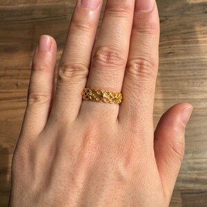 A close-up view of a person's hand wearing a gold ring with an intricate design.