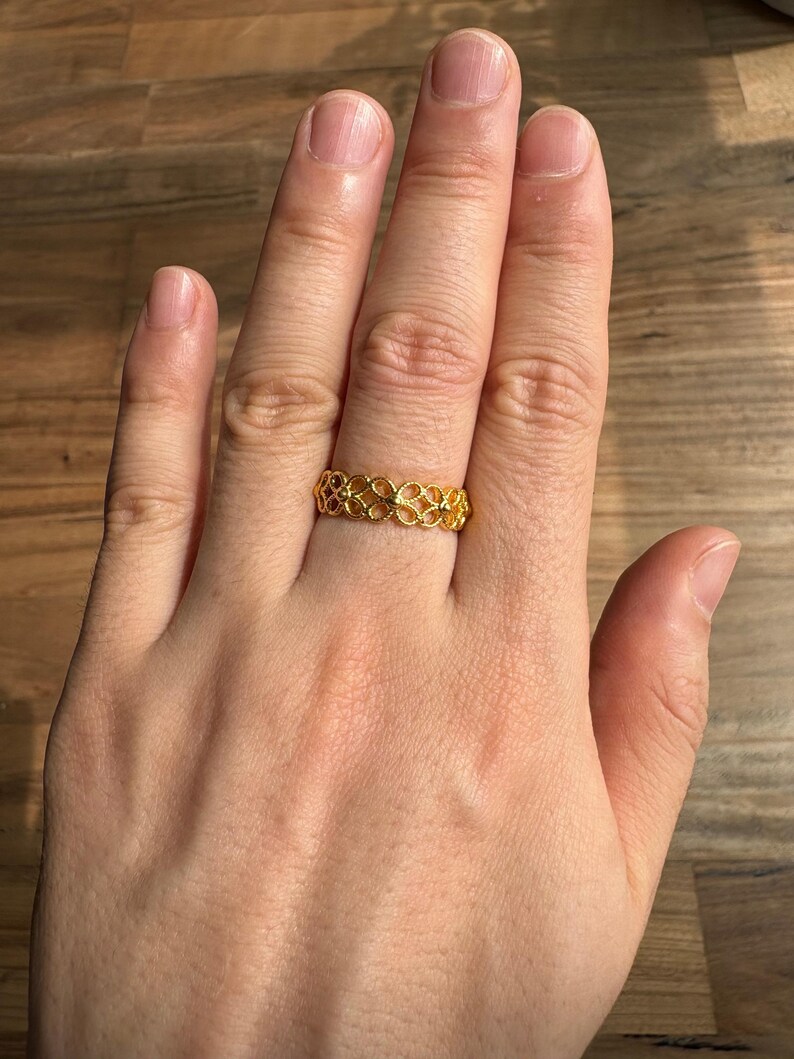 A close-up view of a person's hand wearing a gold ring with an intricate design.