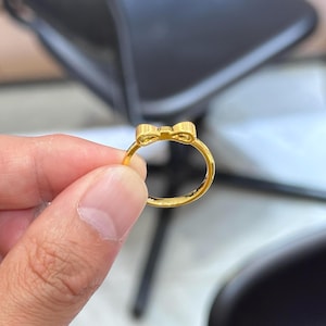 A gold ring with a bow-shaped design is being held in a person's hand.