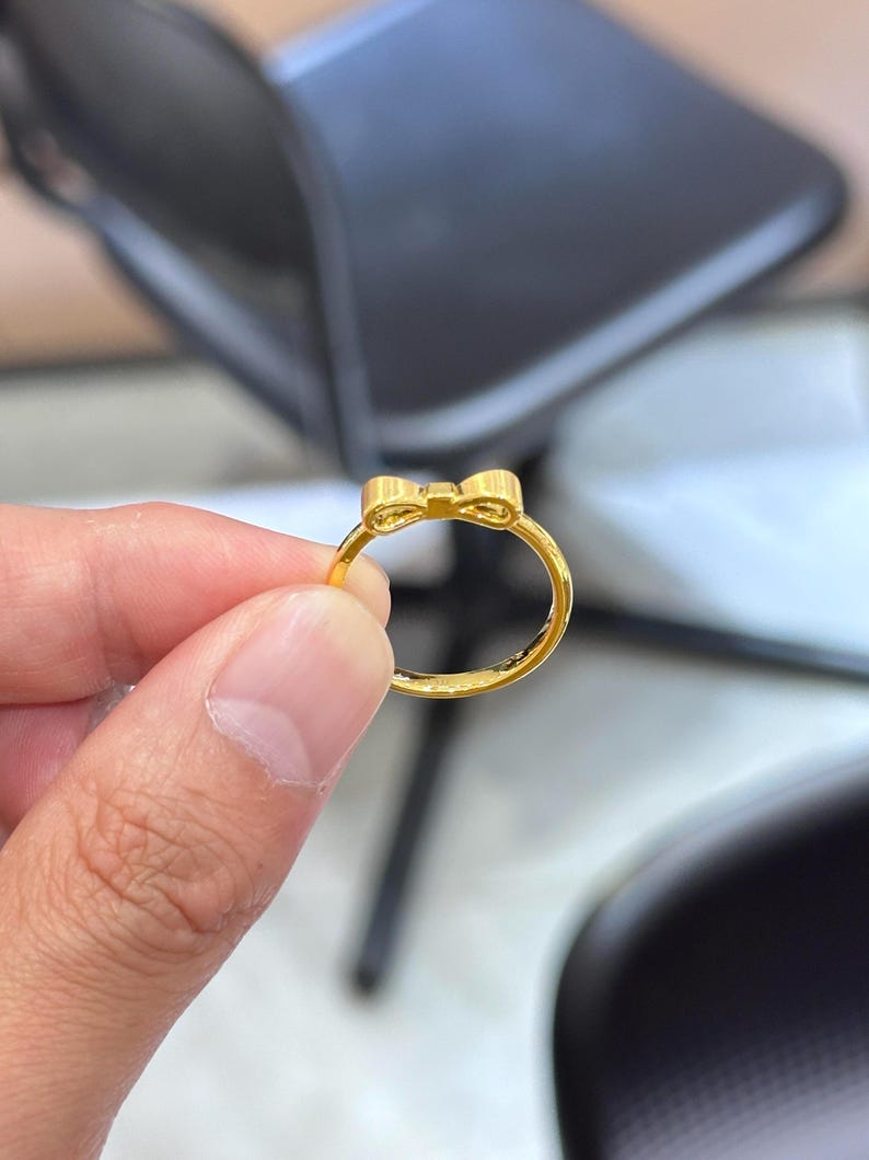 A gold ring with a bow-shaped design is being held in a person's hand.