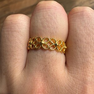 A close-up view of a person's hand wearing a gold ring with an intricate floral design.