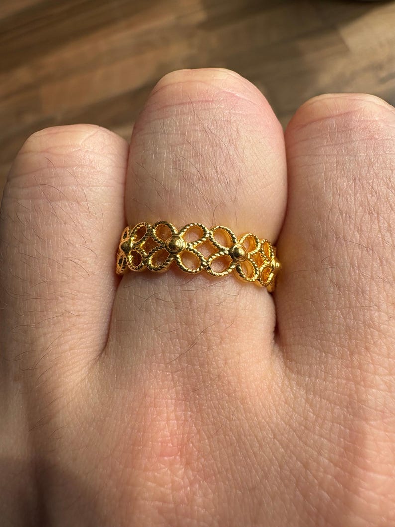 A close-up view of a person's hand wearing a gold ring with an intricate floral design.