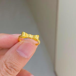 A gold ring with a bow design is being held in a person's hand.