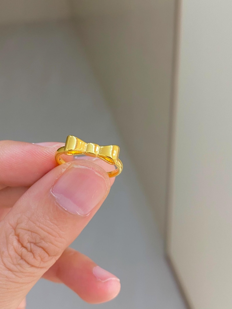 A gold ring with a bow design is being held in a person's hand.