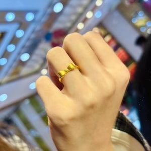 A close-up view of a person's hand wearing a gold ring with a bow design.