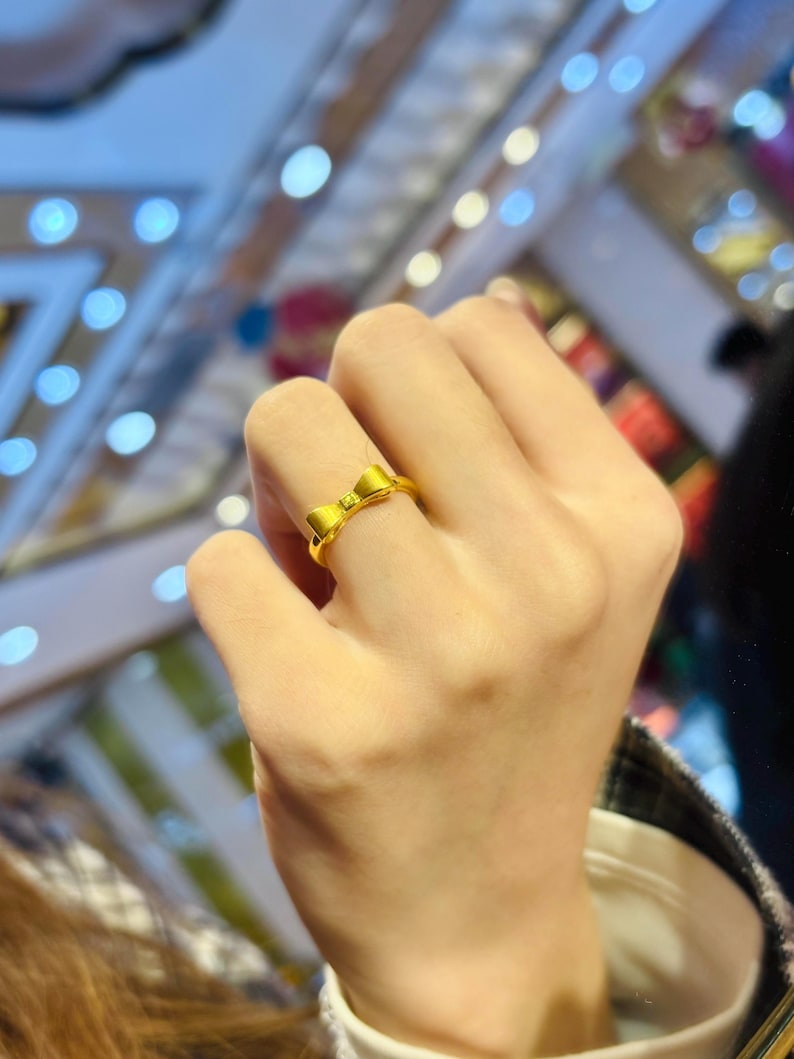 A close-up view of a person's hand wearing a gold ring with a bow design.