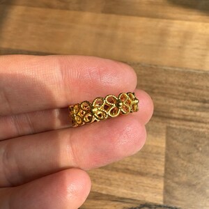 A hand holding a gold ring with an intricate floral design.
