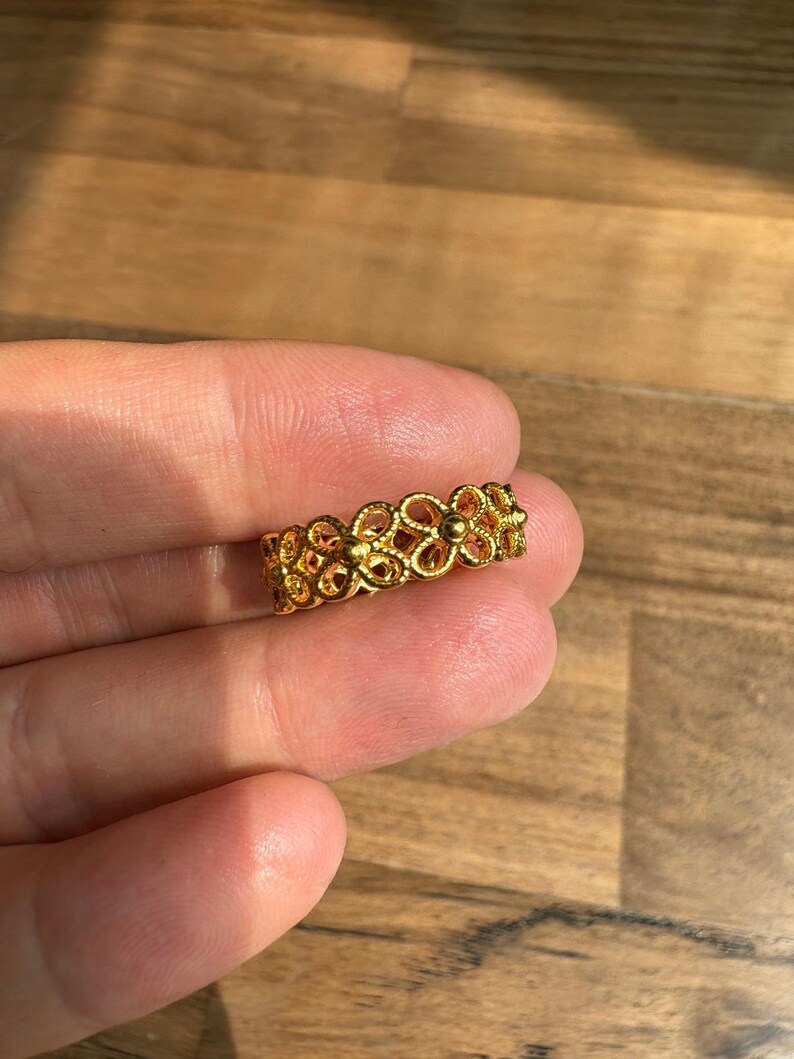 A hand holding a gold ring with an intricate floral design.