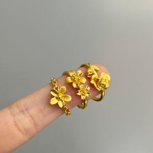 A close-up image of a person's hand wearing three gold-colored flower-shaped rings.