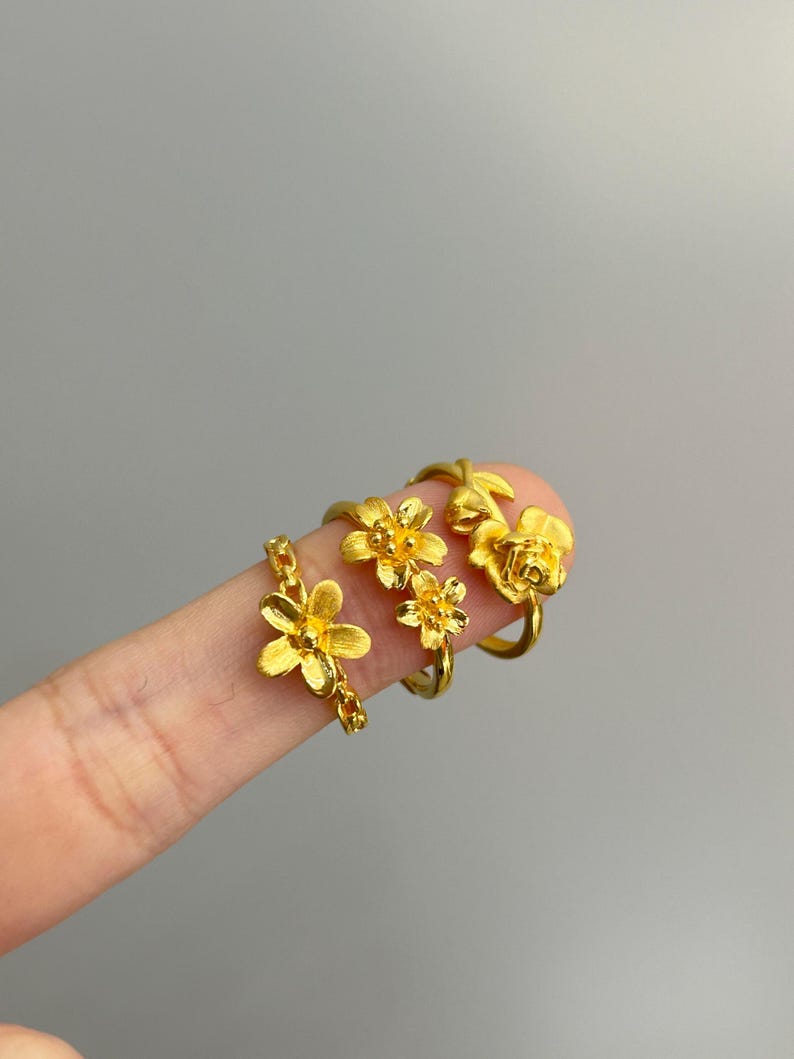 A close-up image of a person's hand wearing three gold-colored flower-shaped rings.