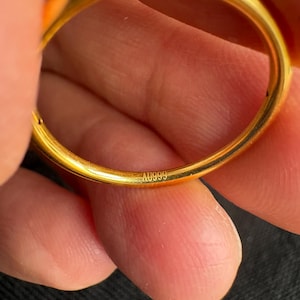 A close-up image of a person's hand holding a gold ring, with the ring's engraving visible.