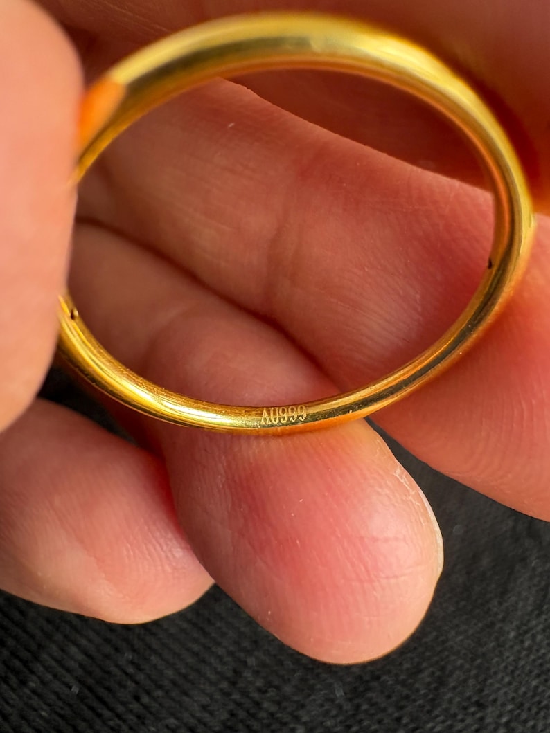 A close-up image of a person's hand holding a gold ring, with the ring's engraving visible.
