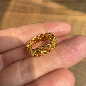 A gold ring with a delicate, intricate design is being held in a person's hand against a wooden background.