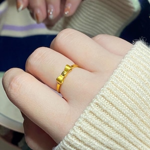A close-up of a person's hand wearing a gold ring with a bow design.