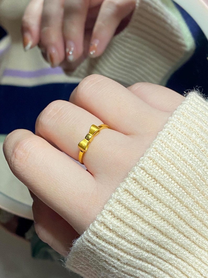 A close-up of a person's hand wearing a gold ring with a bow design.