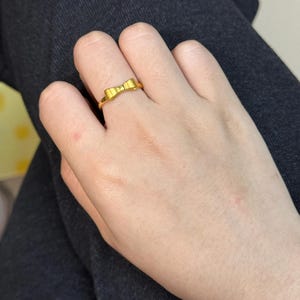 A close-up view of a person's hand wearing a gold ring with a bow design.