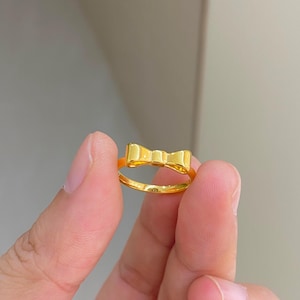 A person's hand holding a gold ring with a bow design.