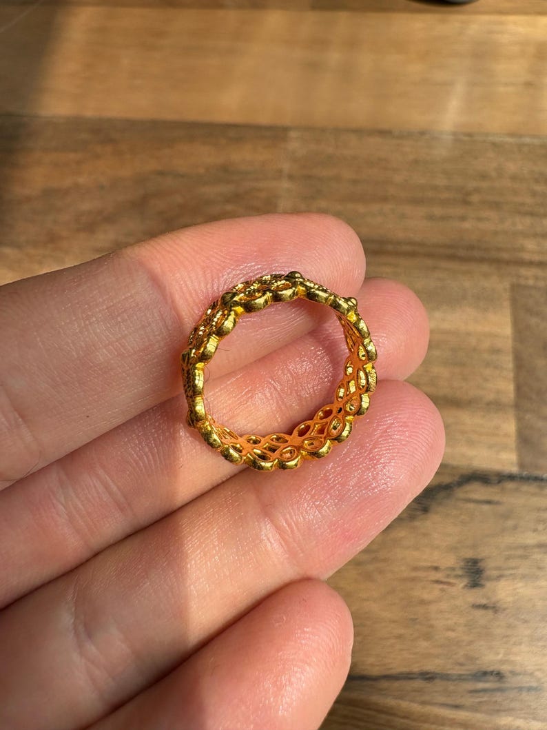 A gold ring is being held in a person's hand against a wooden background.