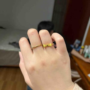 A close-up of a person's hand wearing two rings, one of which is a gold ring with a bow design.