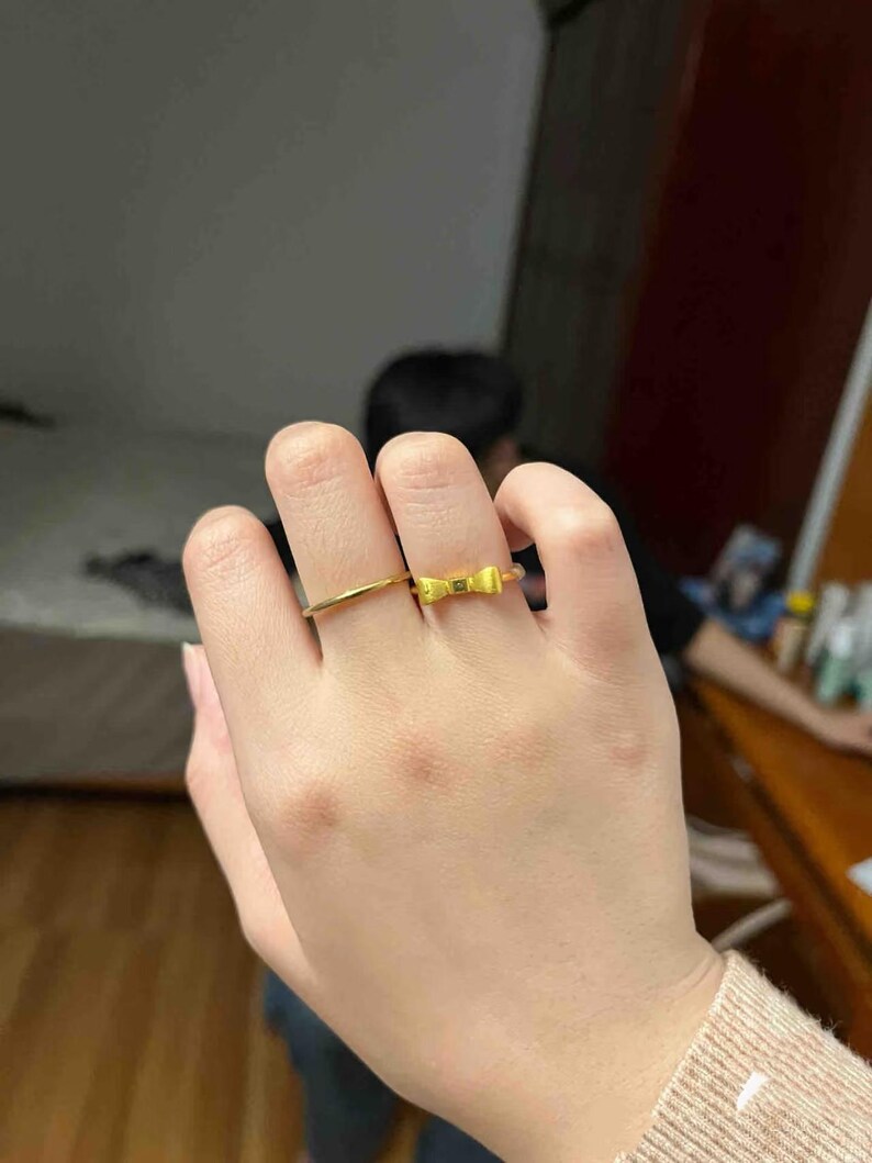 A close-up of a person's hand wearing two rings, one of which is a gold ring with a bow design.