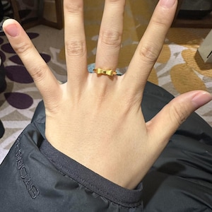 A close-up of a person's hand wearing a gold ring on the ring finger.