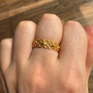 A close-up view of a person's hand wearing a gold ring with a floral design.