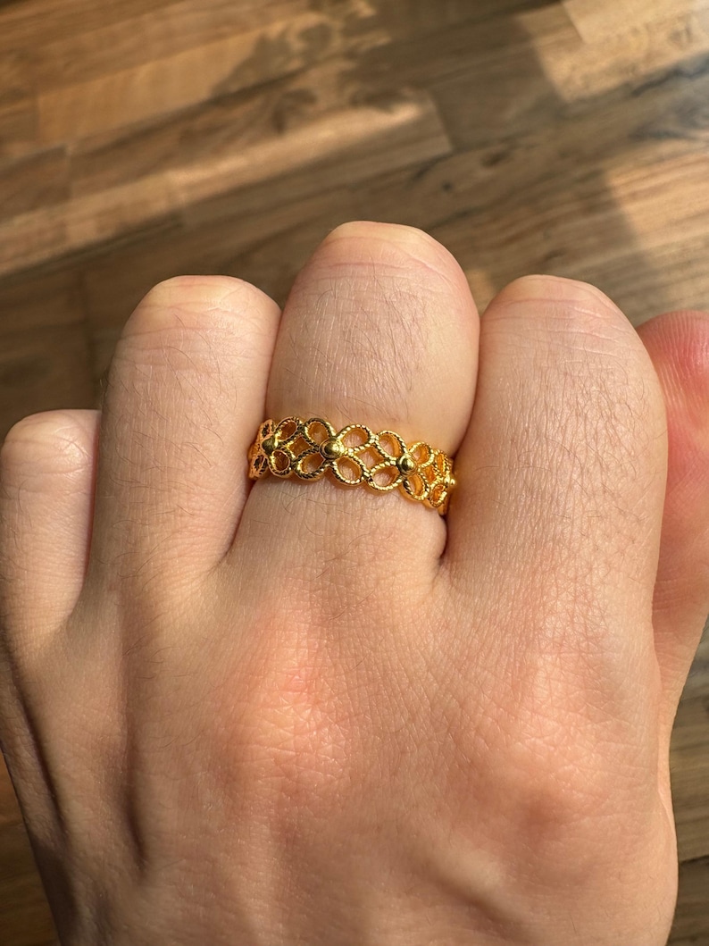 A close-up view of a person's hand wearing a gold ring with a floral design.