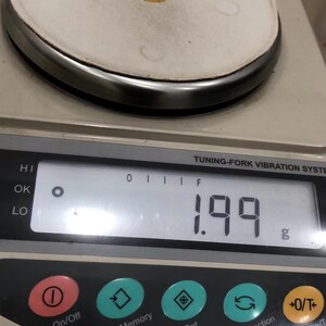 A gold ring is placed on a digital scale, which displays the weight of the ring as 1.99 grams.