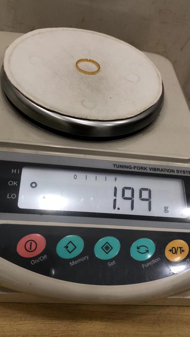 A gold ring is placed on a digital scale, which displays the weight of the ring as 1.99 grams.