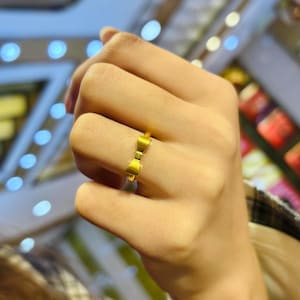 A close-up of a person's hand wearing a gold ring with a bow design.