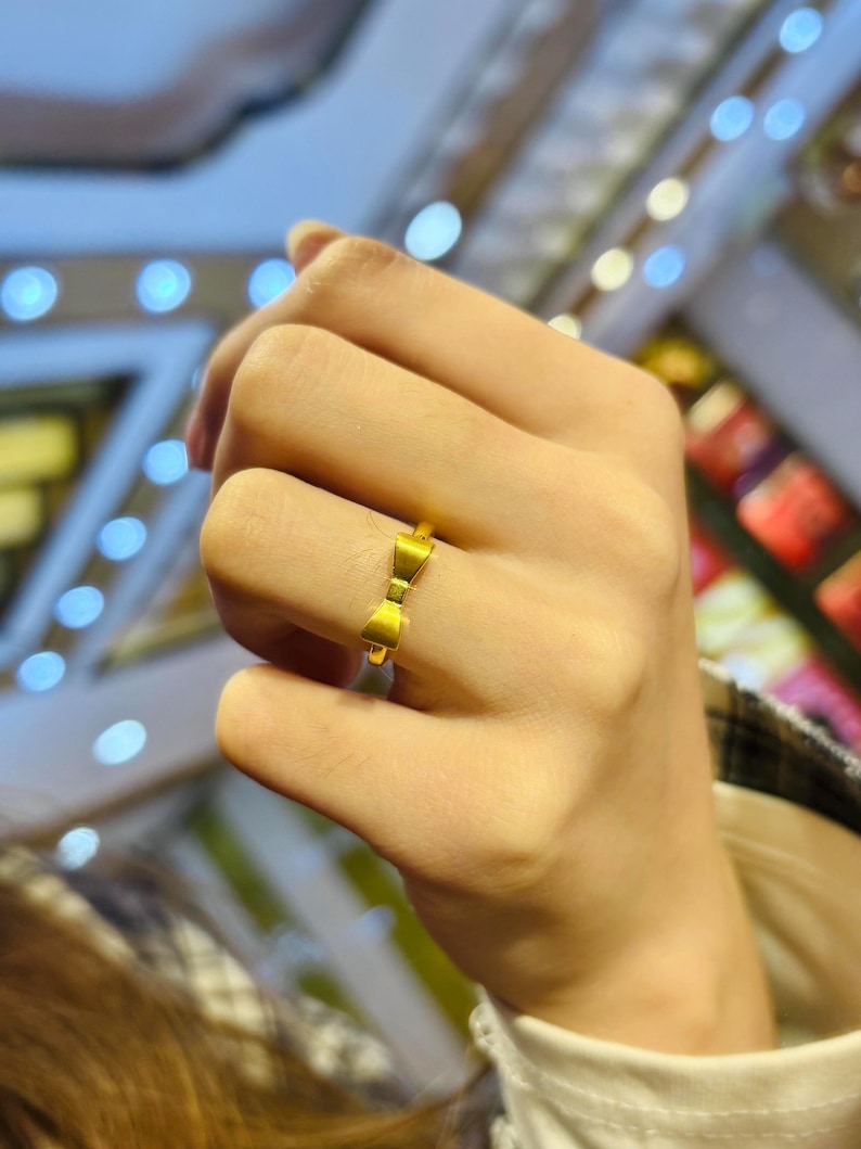 A close-up of a person's hand wearing a gold ring with a bow design.
