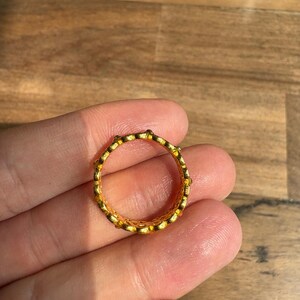 A hand holding a gold ring with a textured design.