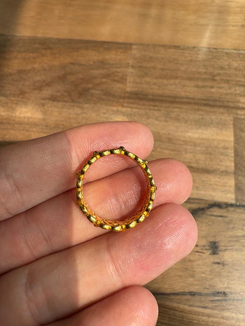 A hand holding a gold ring with a textured design.