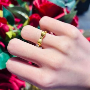 A close-up of a person's hand wearing a gold ring with a bow-shaped design.