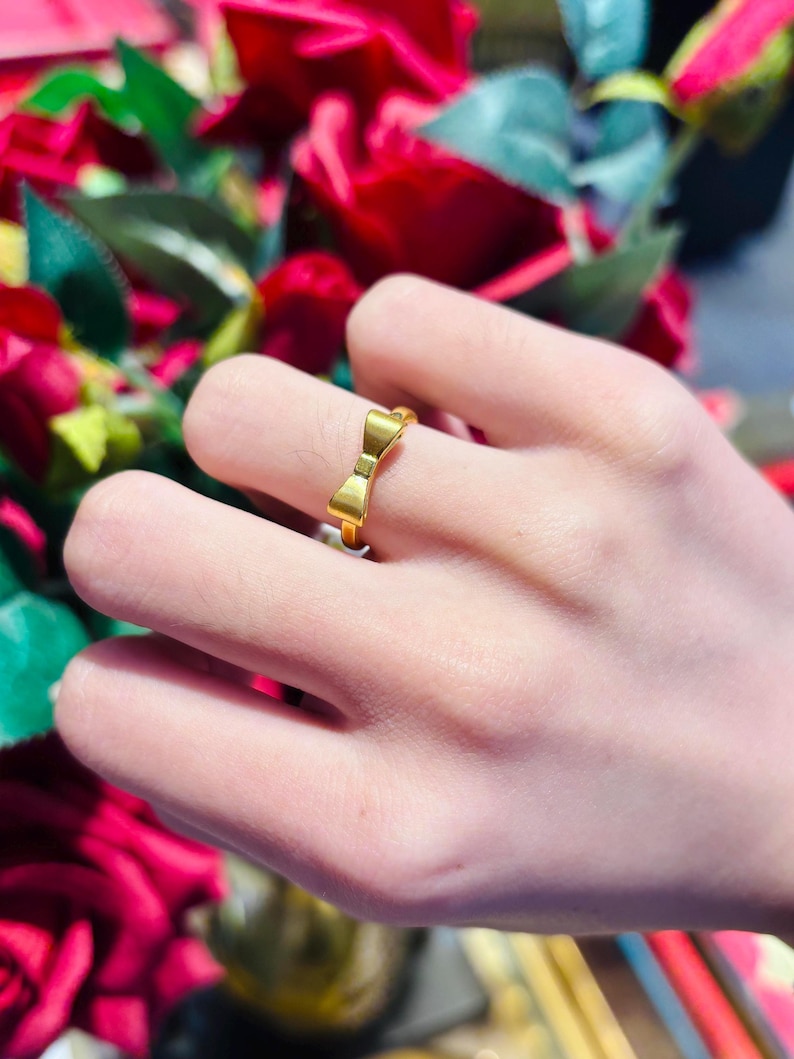 A close-up of a person's hand wearing a gold ring with a bow-shaped design.