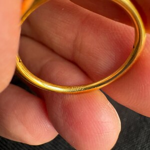 A close-up image of a person's hand holding a gold ring, with the ring's engraving visible.