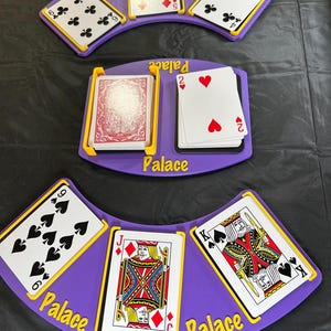 May include: A purple plastic card holder with yellow accents and the word Palace printed on it. The holder displays playing cards including a six of clubs, five of diamonds, four of clubs, two of hearts, six of spades, jack of diamonds, and king of spades.