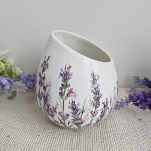 Könnte beinhalten: Weißer Keramikvase mit strukturierter Oberfläche und schräger Öffnung. Die Vase ist mit handgemalten Lavendelzweigen in Lila- und Grüntönen verziert. Ein dekoratives Blumenelement für das Zuhause.
