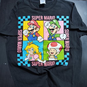 May include: Black t-shirt featuring a colorful Super Mario graphic. The design includes images of Mario, Luigi, Princess Peach, and Toad, set within a checkered border with the words "Super Mario".