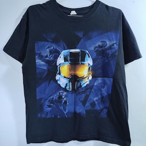 May include: Black t-shirt featuring a graphic of a futuristic helmet with a yellow visor, surrounded by blue geometric shapes and figures. The design is centered on the front of the shirt, with a crew neck and short sleeves.
