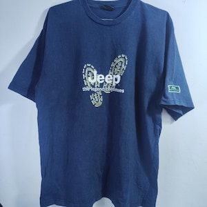 May include: Dark blue t-shirt with the Jeep logo and the words "the legend continues" in light green. The shirt has short sleeves and a small Jeep logo patch on the left sleeve.