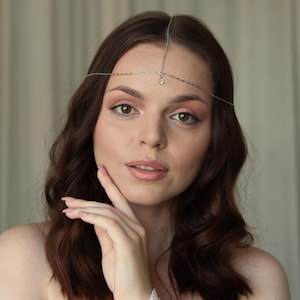 Puede incluir: Un adorno para la cabeza plateado con un delicado diseño de cadena. El adorno para la cabeza presenta una pequeña gema transparente en el centro de la frente. La joya está diseñada para ser usada como accesorio para el cabello.