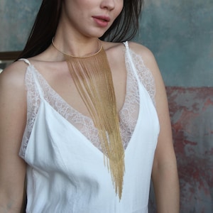 Può includere: Una collana dorata con un design a colletto e frange a catena a cascata. La collana è un pezzo forte, che aggiunge un tocco di glamour. Le catene sbiadiscono gradualmente nel colore, creando un effetto sfumato. È un accessorio di moda.