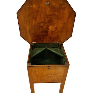 Può includere: Un contenitore in legno con coperchio ottagonale aperto. La scatola è realizzata in legno marrone chiaro e ha un interno in feltro verde. La scatola è rettangolare con quattro gambe e un piccolo chiavistello.