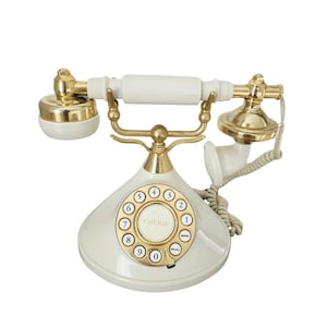 Könnte beinhalten: Cremefarbenes Vintage-Wählscheibentelefon mit goldfarbenen Akzenten. Das Telefon hat ein kreisförmiges Zifferblatt mit Zahlen und dem Wort "CHERIE" in der Mitte. Hörer und Basis sind cremefarben.