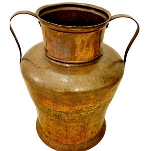 Op de afbeelding: Een gehamerde koperen vaas met een brede basis en een kleinere, cilindrische bovenkant. De vaas heeft twee gebogen handvatten en een rijke, verouderde patina. De algehele vorm doet denken aan een traditionele waterkan.